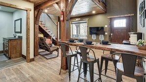 Una cucina rustica con travi in legno, un angolo bar con sgabelli e una scala che conduce a un livello superiore.