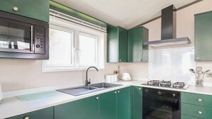 A kitchen with green cabinets, a black oven, a stainless steel sink, and a window with blinds. - 2 bedroom accommodation in Caersws (Caersws)
