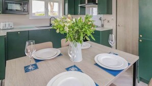 A modern kitchen with green cabinets, a microwave, a toaster, and a dining table set for two with plates, glasses, and a vase of flowers. - 2 bedroom accommodation in Caersws (Caersws)