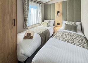 Habitació d'hotel amb dos llits, un armari de fusta, una finestra amb cortines i una làmpada penjant a la paret.