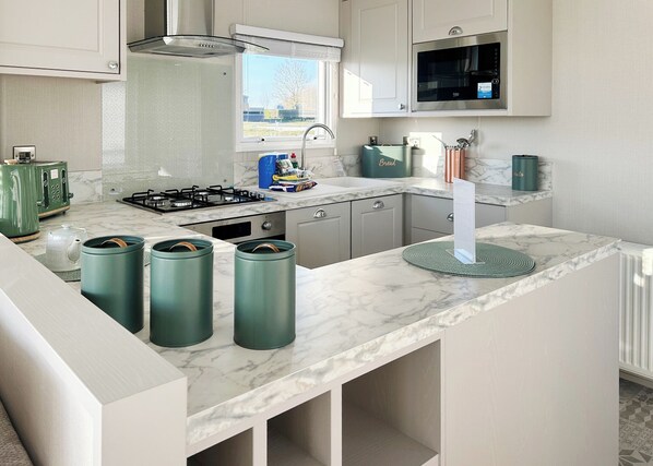 A modern kitchen with a gas stove, a microwave, and green storage containers.