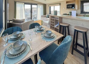 Uma sala de jantar com mesa posta para quatro, cadeiras, uma cozinha com micro-ondas e vista para o exterior.