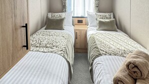 A bedroom with two beds, a wooden wardrobe, a nightstand, and a window with curtains.