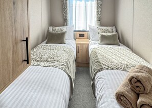 A bedroom with two beds, a wooden wardrobe, a nightstand, and a window with curtains.