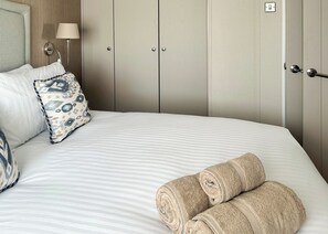 Una cama bien hecha con una colcha a rayas, dos almohadas con un diseño estampado y toallas enrolladas sobre la cama.
