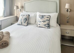 A neatly made bed with two patterned pillows, a bedside table with a lamp, and a wall-mounted light fixture.