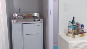 Eine kleine Küche mit Spüle, Herd und Kühlschrank. Auf der Arbeitsfläche steht ein Korb mit Wasserflaschen und Snacks.