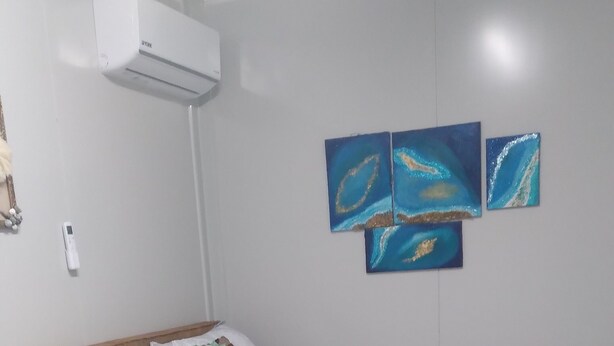 Ein Schlafzimmer mit einem Bett, einem kleinen runden Tisch, einem Stuhl, einer Klimaanlage und einem an der Wand montierten Thermostat.