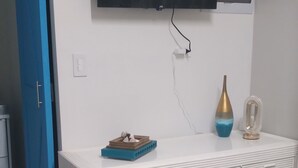 Een witte kast met lades, een wandtelevisie, een vaas en een decoratief object erboven.