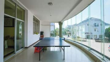 A room with a ping pong table, large windows, and a view of buildings outside.