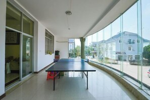 Een kamer met een tafeltennistafel, grote ramen en uitzicht op gebouwen.