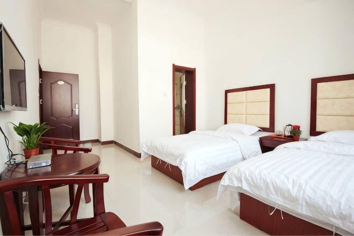 Habitación de hotel con dos camas, un escritorio, una silla, un televisor y una puerta.