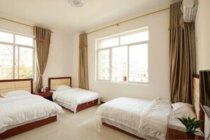 A hotel room with three beds, large windows, a flat-screen TV, and a potted plant.