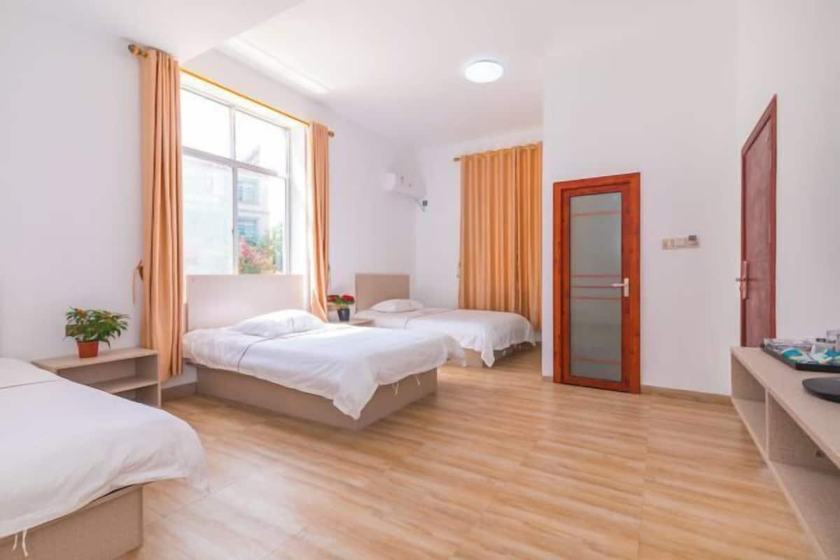 Un dormitorio con dos camas, piso de madera, ventana con cortinas y puerta con panel de vidrio esmerilado.