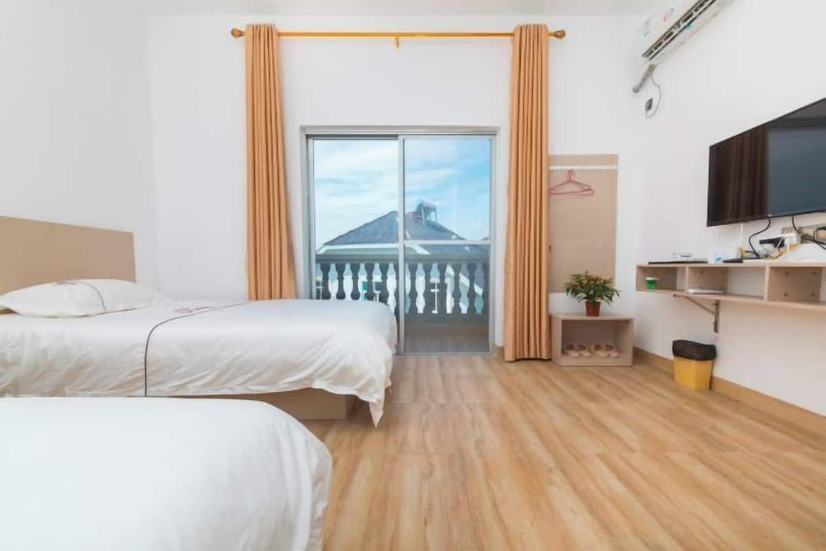 Habitación de hotel con dos camas, televisión, un estante con objetos y un balcón con cortinas.