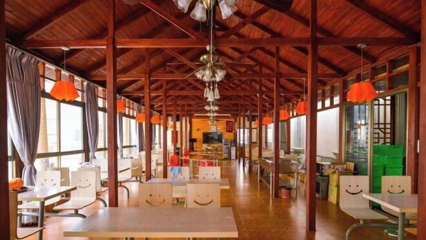 A spacious room with wooden beams, tables with smiley face cutouts, orange pendant lights, and large windows. - OYO Beihai Jinghai Villa (Yintan) (Beihai)