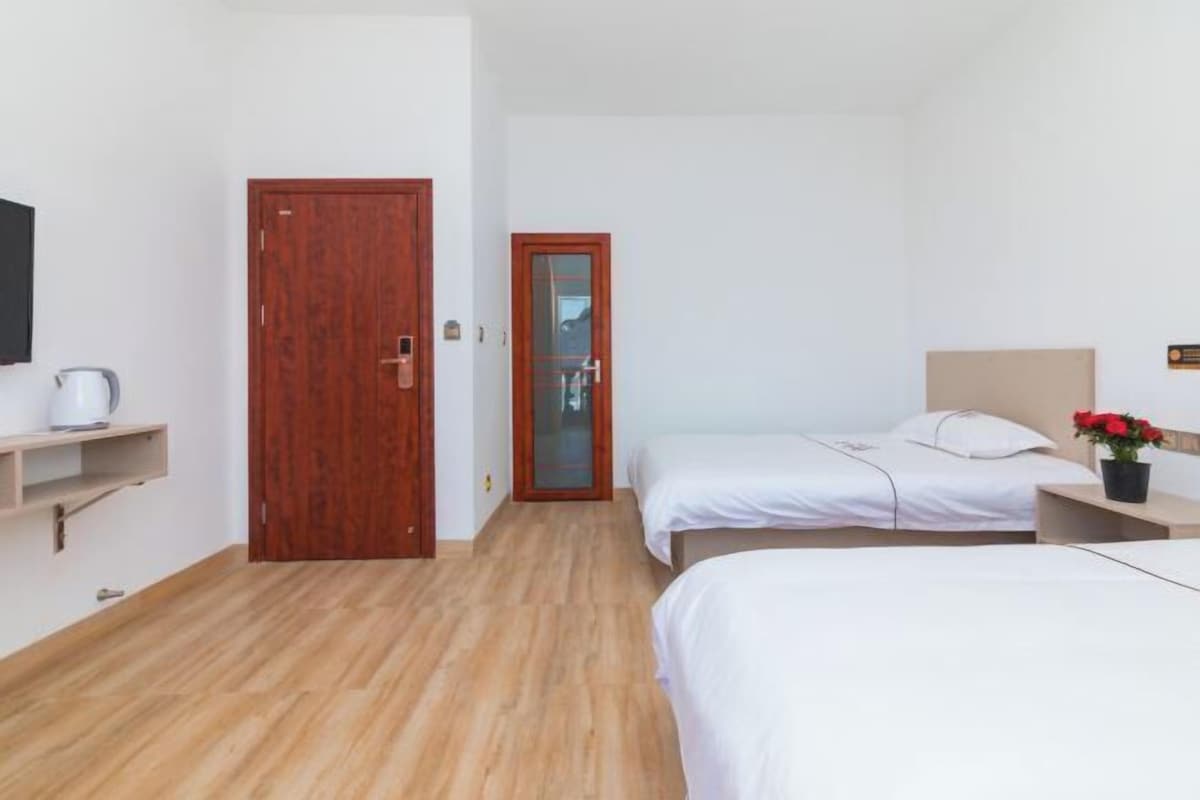 A hotel room with two beds, a wooden floor, a small shelf with a kettle, and a wooden door.