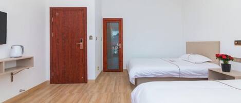 A hotel room with two beds, a wooden floor, a small shelf with a kettle, and a wooden door.