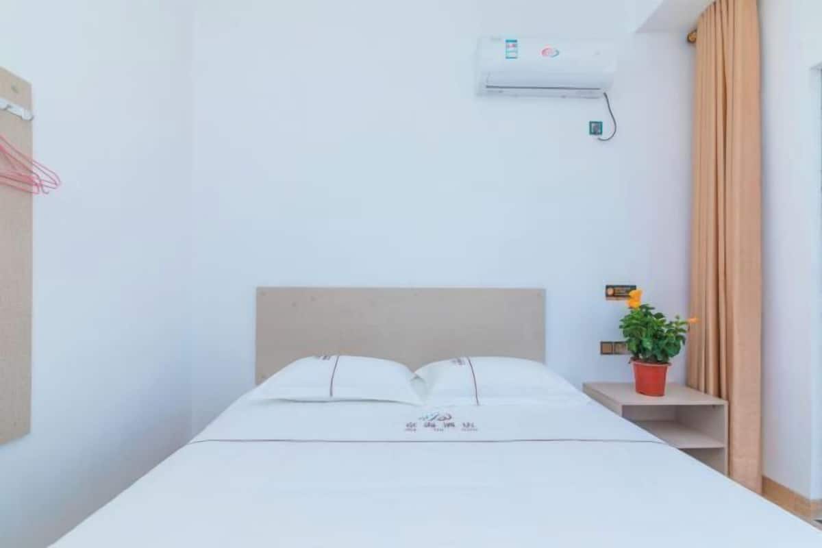 Una cama individual con cabecera de madera, una mesita de noche pequeña con una maceta roja y un equipo de aire acondicionado en la pared.
