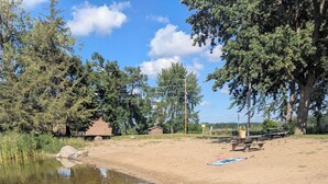 A clear water body with a sandy shore, surrounded by trees and a picnic area.