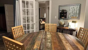 A round wooden dining table with four chairs, a globe, and a lamp on a side table in a room with a door and a mirror on the wall.
