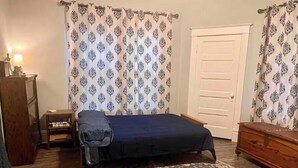 A room with a bed, a wooden dresser, a nightstand, a patterned rug, and curtains with a geometric design.