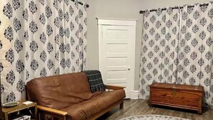 A living room with a brown leather sofa, a wooden side table, a patterned rug, and a wooden dresser.