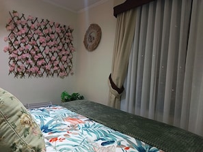 A bedroom with a bed, a decorative wall panel, a mirror, and a window with curtains.