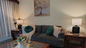 Ein Wohnzimmer mit einer Couch, zwei Beistelltischen mit Lampen, einem Glastisch mit Dekoration und einem Gemälde an der Wand.