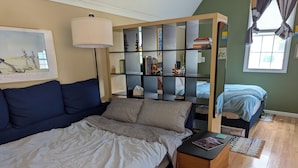 A bedroom with a bed, a sofa, a bookshelf, and a window. - Tiny, Funky, and Full of Love - Welcome to the Love Shack (Piney Point)