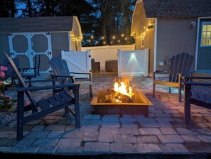 A backyard with a fire pit, outdoor seating, and string lights.
