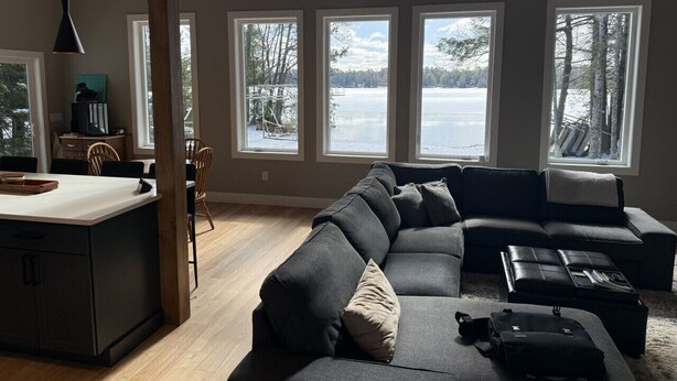A modern living room with a large sectional sofa, a dining area with a wooden table, and a kitchen with a white countertop. - Serendipity North Three Lakes (Three Lakes)