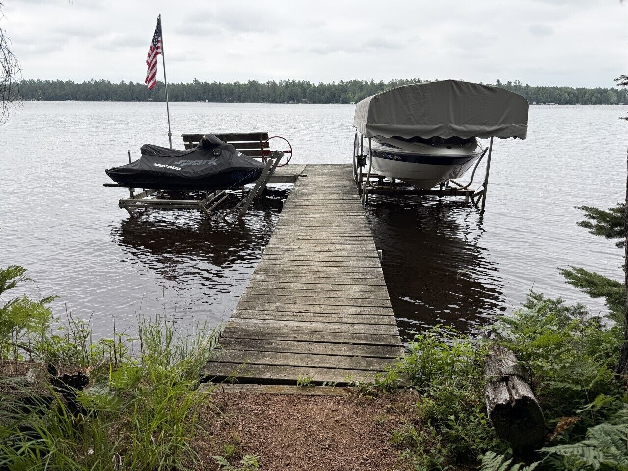Une jetée en bois s’avance sur un lac paisible, avec un bateau à moteur abrité et un kayak amarrés sur la jetée.