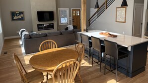 A modern living space with a wooden dining table, grey sofa, and a kitchen island. - Serendipity North Three Lakes (Three Lakes)