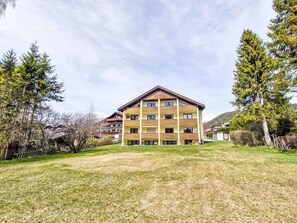 Un immeuble à plusieurs étages, doté d’un toit plat, entouré d’arbres et bordé d’une zone herbeuse.