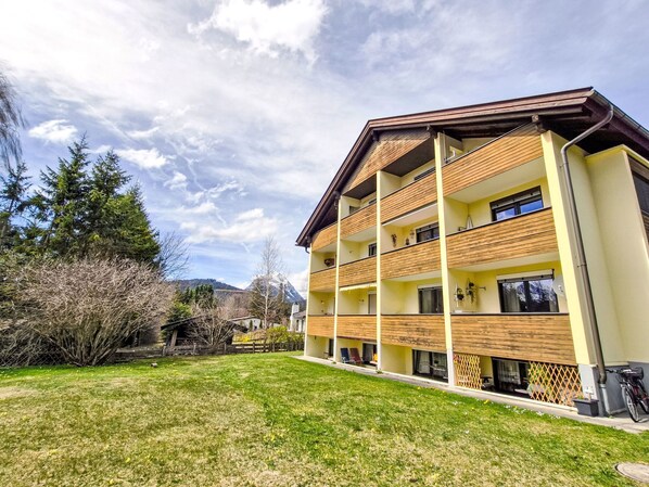 Un immeuble à plusieurs étages doté de balcons, d’une pelouse verdoyante et d’arbres.