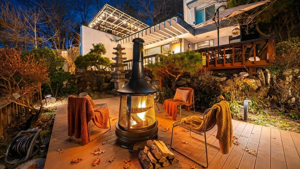 Un edificio moderno con un jardín japonés tradicional, un farol de piedra y una terraza de madera con sillas.