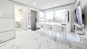 A modern kitchen with white cabinetry, a marble floor, and a dining area with white chairs and a table.