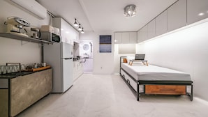 Een compacte, moderne kamer met kitchenette, een bed met houten hoofdbord en een klein bureau.