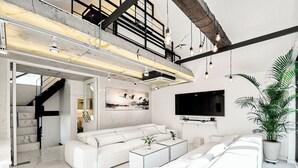 Un salon moderne avec un canapé d’angle, un téléviseur à écran plat et un escalier menant à un niveau supérieur.