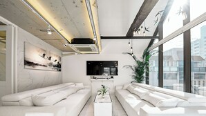 Un salon moderne doté d’un grand canapé, d’une table basse, d’un téléviseur à écran plat et d’une grande fenêtre donnant sur la ville.