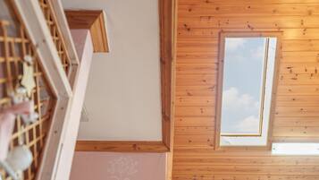 Une pièce avec des poutres apparentes en bois au plafond, une lucarne et une vue sur le ciel.