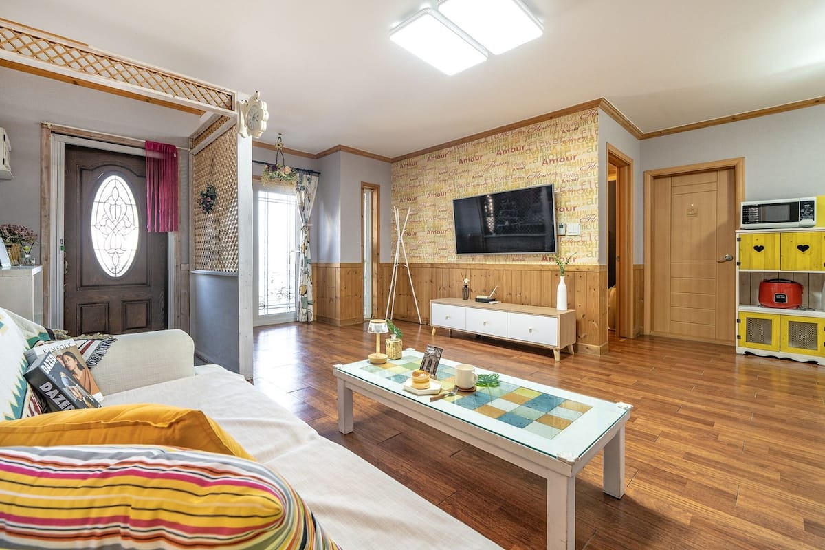 Una sala de estar acogedora con un sofá, una mesa de centro y un televisor. Se aprecia un armario de madera y un mueble de almacenamiento amarillo.