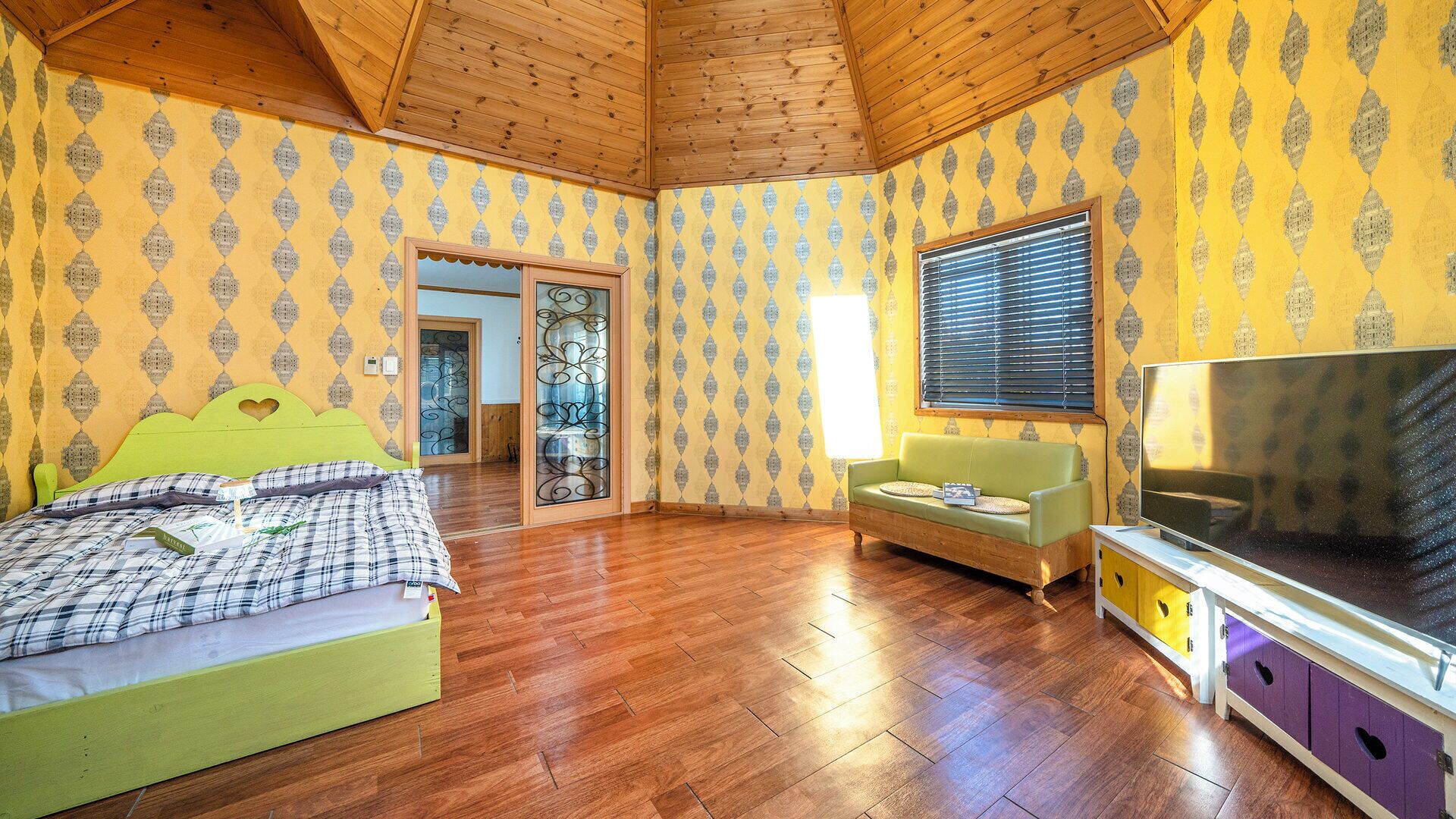 A room with a bed, a sofa, a TV, and a wooden ceiling.