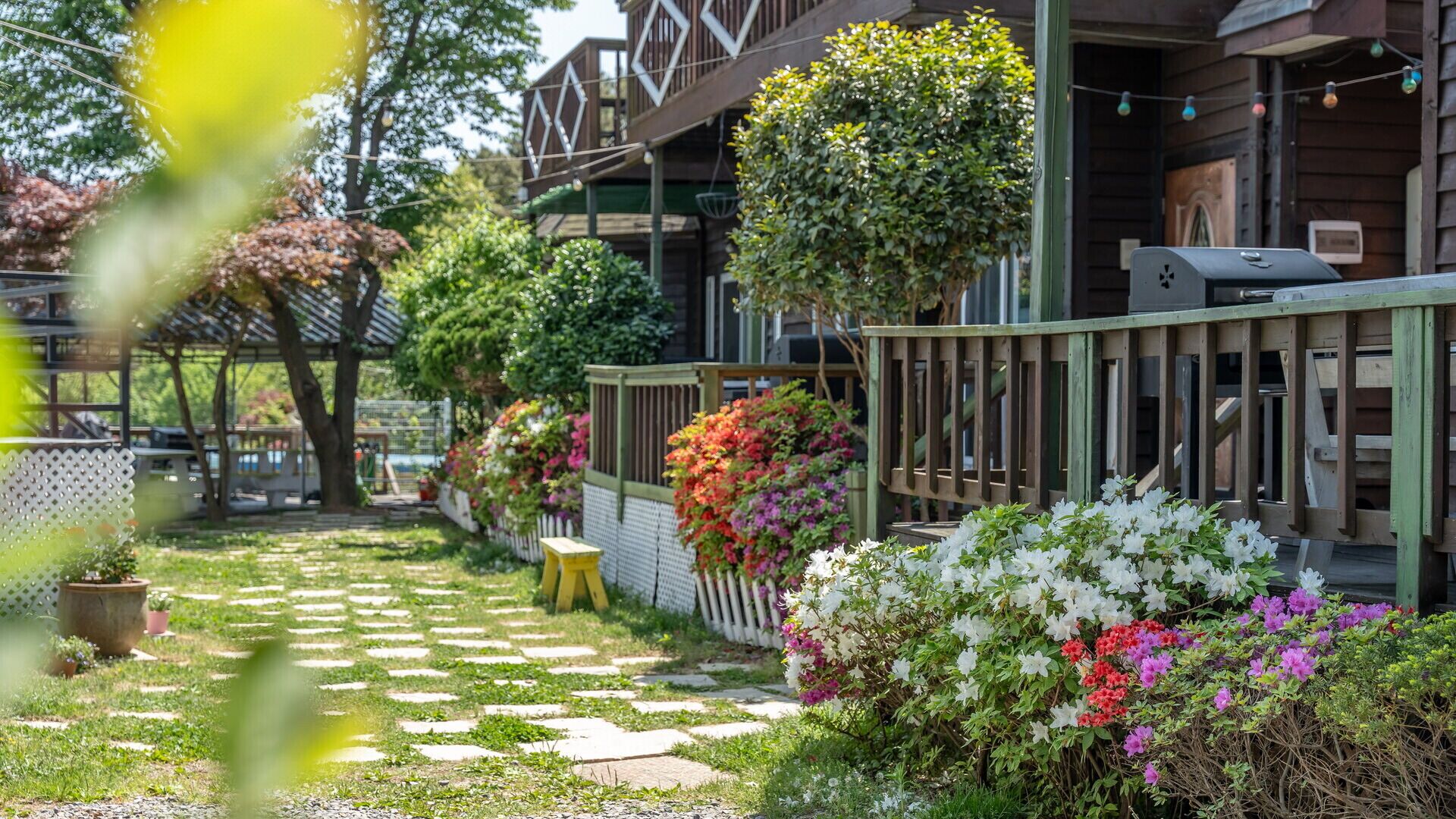 A garden pathway leading to a wooden building with hanging flower baskets and a barbecue grill.