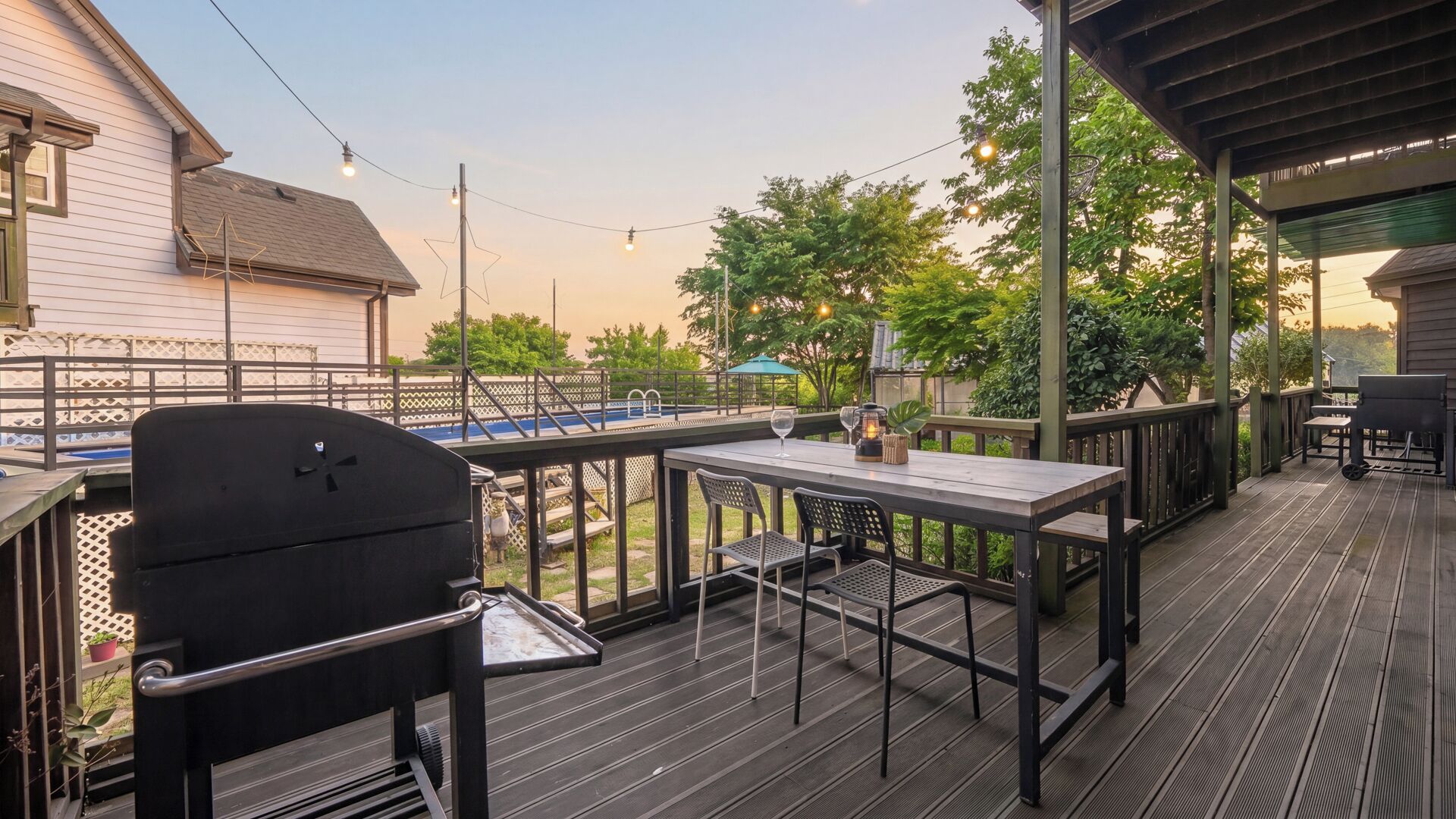 Une terrasse extérieure couverte, équipée d’un barbecue, de tables et de chaises, et offrant une vue sur une piscine et des arbres.