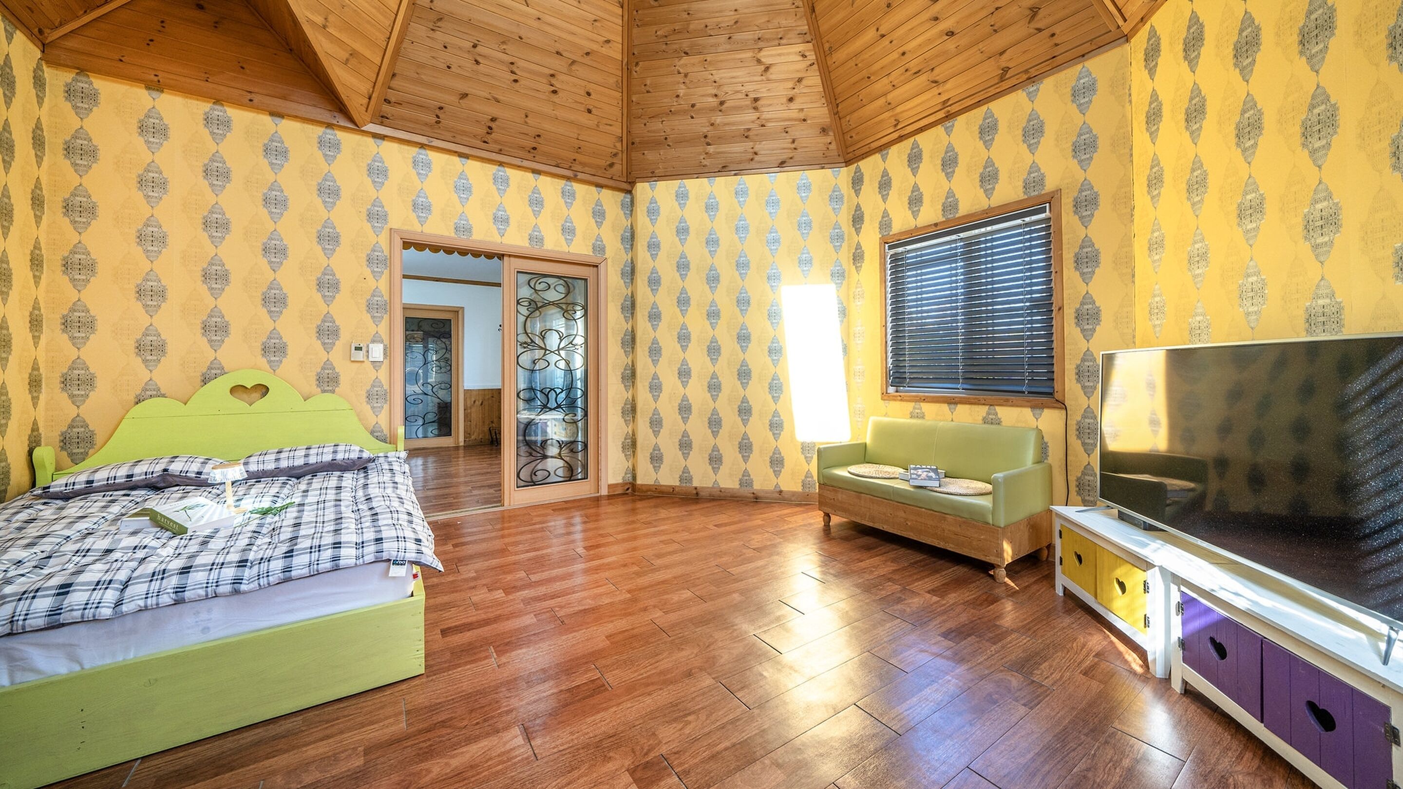 Een kamer met een bed, een bank, een televisie en een houten plafond.