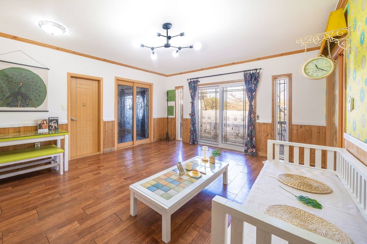 Amplio salón con piso de madera, una mesa de centro, un banco y una mesa de comedor con individuales.