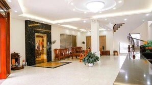 A spacious lobby with a marble reception desk, wooden chairs, a large potted plant, and a staircase leading to upper floors. - Kinh Bac Hotel Hai Tien (Hoang Thanh)