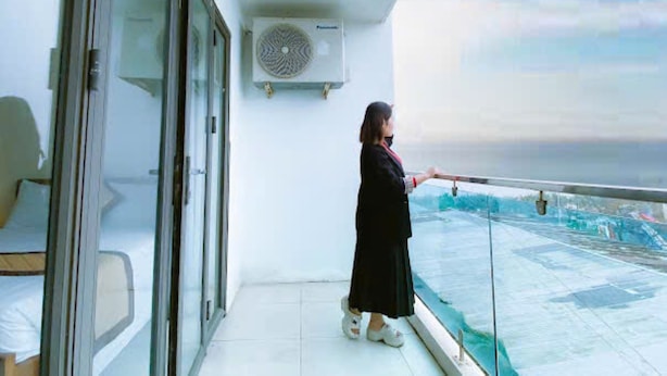 A balcony with a glass railing, a person standing, and a view of the sea. - Kinh Bac Hotel Hai Tien (Hoang Thanh)